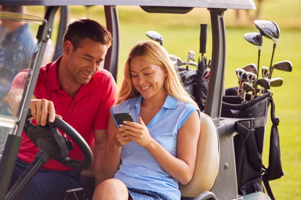 casal sentado em buggy de golfe em curso com mulher usando celular - golf course golf people sitting - fotografias e filmes do acervo