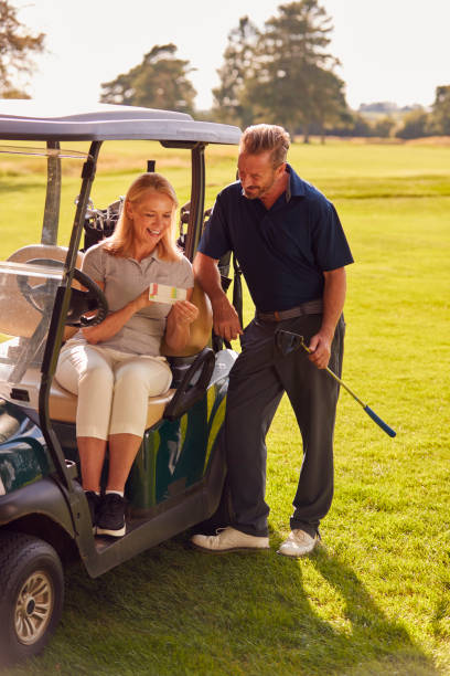 mature couple sitting in buggy playing round on golf and checking score card together - golf course golf people sitting imagens e fotografias de stock