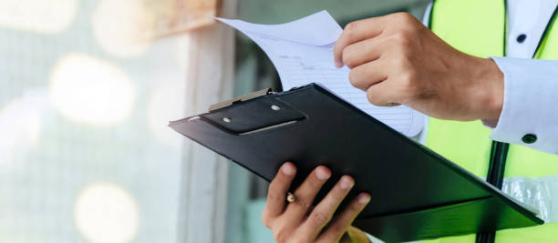istock Renovation. home inspector engineer in green reflective jacket checking review document and inspecting with clipboard at construction site building, construction, contractor and engineering concept 1356334565