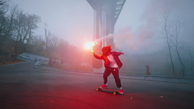 Skater performs a tail turn trick while holding a torch in one hand. Young man riding a skateboard at night with a red burning signal flare in his hand, dangerous stunts