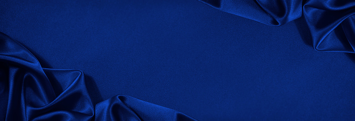 Beautiful dark blue silk satin background. Soft folds on shiny fabric. Luxury background with copy space for text, design. Wide banner. Flat lay, top view. Birthday, Christmas, Valentine.