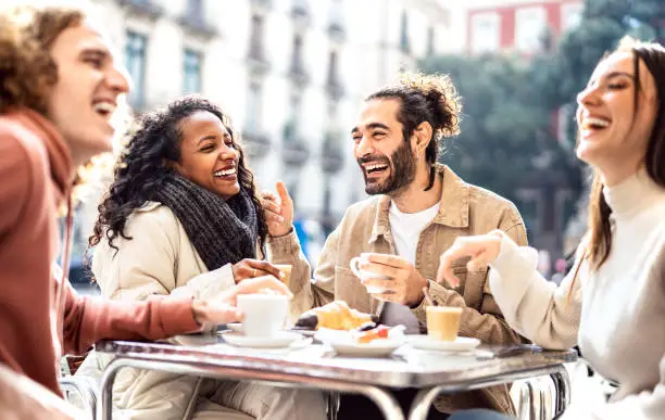Photo of People group drinking cappuccino at coffee bar patio - Friends talking and having fun together at sidewalk cafeteria - Life style concept with happy men and women at cafe dehor - Warm bright filter