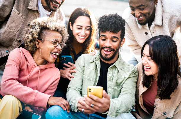 amigos multiculturales divirtiéndose con el teléfono móvil en el patio de la universidad del campus - hombres y mujeres jóvenes que pasan tiempo juntos compartiendo videos divertidos en un dispositivo de teléfono inteligente - filtro vívido con enfoq - nativo digital fotografías e imágenes de stock