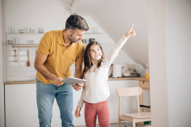 istock Little girl and her dad using a digital tablet to adjust home smart system 1356338758
