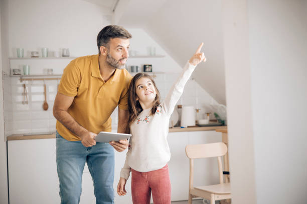 Man and his little daughter turning on the lights using a home smart system Mid adult man and his little daughter setting up the home smart system using a digital tablet. smart home family stock pictures, royalty-free photos & images