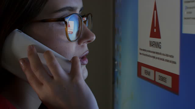 Warning on computer screen, phone support. Young woman wearing glasses.