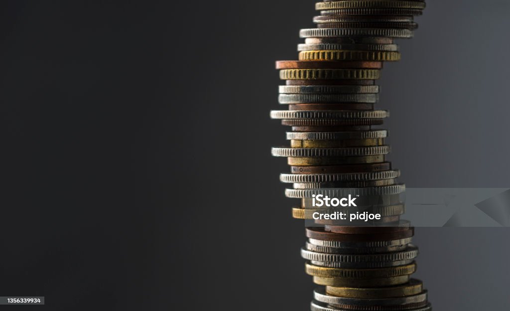 Stack of coins, studio shot. Large stack of international coins against a grey background. Inflation - Economics Stock Photo