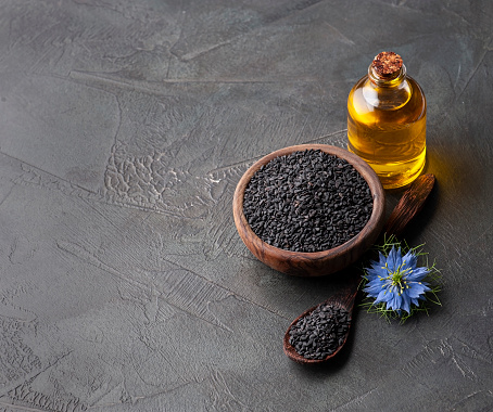 Glass bottle of black cumin  oil and cumin seeds on concrete backgrounds. Homeopathy.