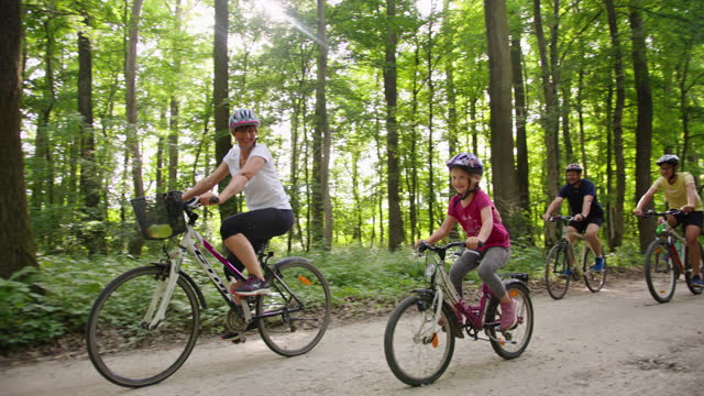 Slow motion shot of a family with three children rides bicycles on a road through a green forest.