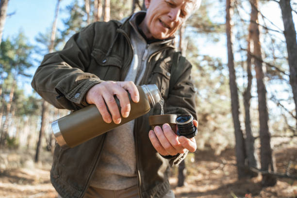 istock Old man pouring hot beverage to the cup from the thermos while resting 1356343586