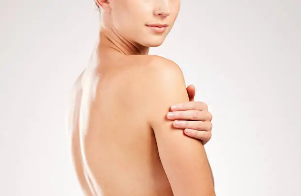 Photo of Studio shot of an unrecognizable young woman touching her shoulder while posing against a grey background