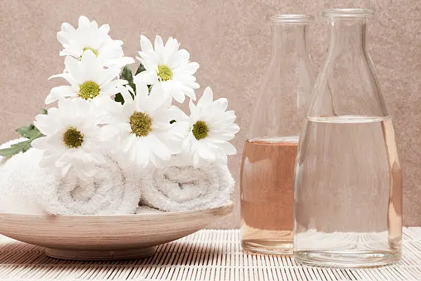 bottles with fragrance beside white towels and bunch of margarite flowers