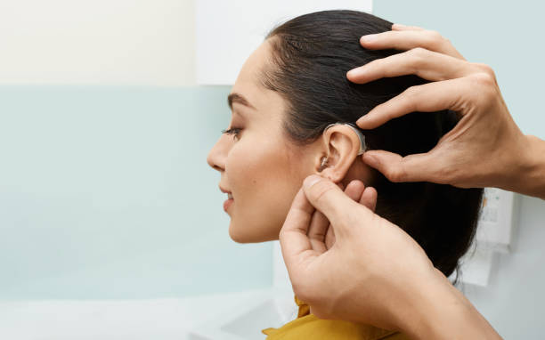 Installation hearing aid on woman's ear at hearing clinic, close-up, side view. Deafness treatment, hearing solutions Installation hearing aid on woman's ear at hearing clinic, close-up, side view. Deafness treatment, hearing solutions hearing loss photos stock pictures, royalty-free photos & images