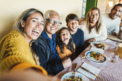 Happy latin family doing selfie while eating together at home - Focus on mother face