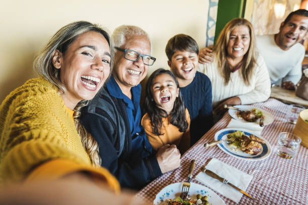 Happy latin family doing selfie while eating together at home - Focus on mother face stock photo