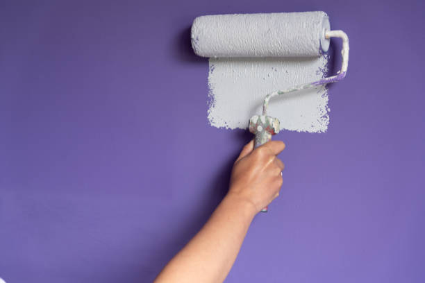 istock Woman hand applying light color paint to wall with roller 1356352739