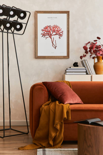 istock Creative composition of stylish living room interior with mock up poster frame, orange sofa, beige commode, coffee table and stylish personal accessories. Artistic space. Template. 1356352908