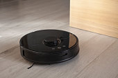 Black robot vacuum cleaner on white wooden floor.