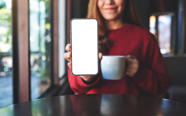 istock A woman holding and showing a mobile phone with blank white screen while drinking in cafe 1356353551