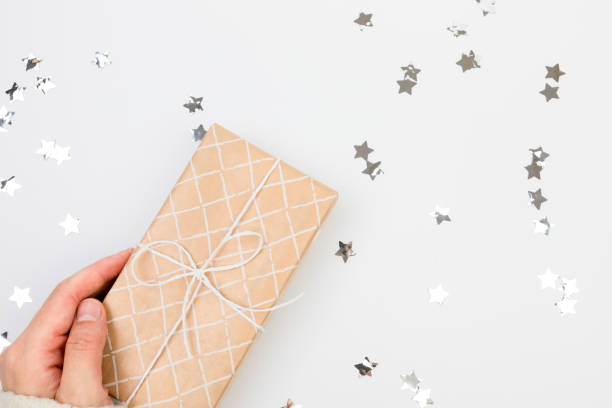 istock gifts or presents boxes silver confetti on white table top view. female hands in a warm sweater are holding a gift 1356355332