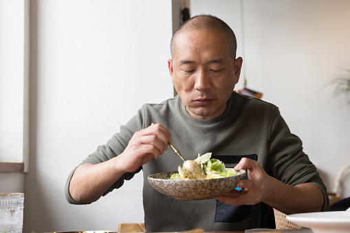A middle-aged Asian man eats a vegetable salad in a restaurant