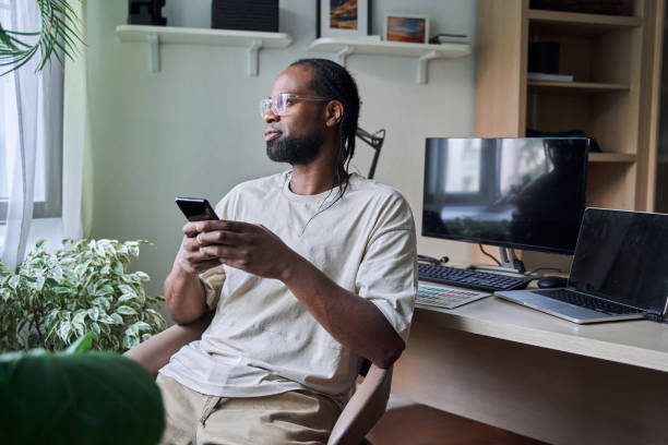 istock Male person holding smartphone and looking at the window while relaxing 1356356577