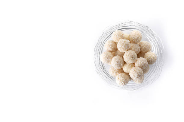 Round candies in a white plate covered with coconut shavings on a white background and with a red heart.