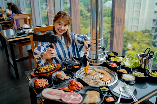 Active woman holding a tripod professionally reviewing the taste of food in a Korean-style restaurant.