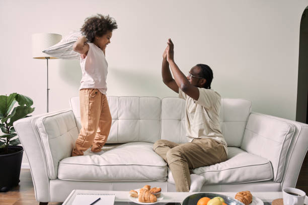 istock Outgoing dad having fun with his little curly daughter while sitting on cozy sofa 1356356689