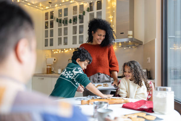 schwester und bruder machen weihnachtshafte lebkuchenplätzchen mit einer mutter - two parent family indoors home interior domestic kitchen stock-fotos und bilder