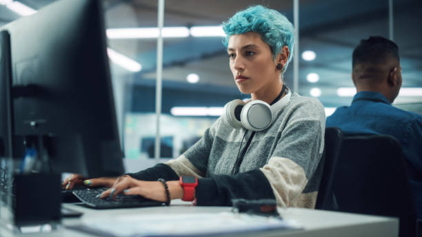 多様な多民族オフィスで:デスクトップコンピュータ上で働く若いスタイリッシュな女性の肖像画。現代コンテンツを作成する非バイナリの人, 現代のプロジェクトデザインを行います, カラ� - ウェブデザイナー ストックフォトと画像