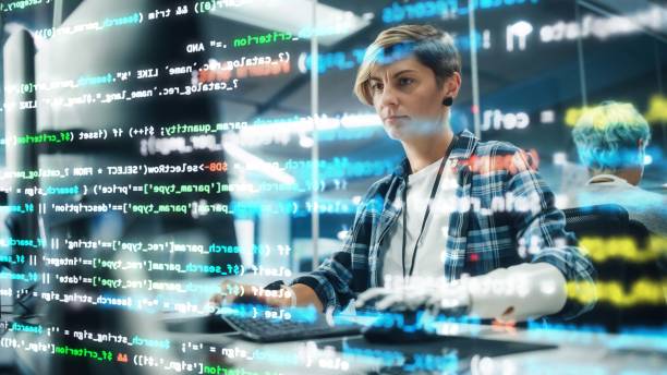 istock Shot with Visualisation of Running Computer Code on Foreground. Portrait of Motivated Woman with Disability Using Prosthetic Arm to Work on Computer in Body Positive Office. Myoelectric Bionic Hand 1356364161