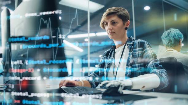 istock Shot with Visualisation of Running Computer Code on Foreground. Portrait of Motivated Woman with Disability Using Prosthetic Arm to Work on Computer in Body Positive Office. Myoelectric Bionic Hand 1356364166