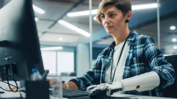 Diverse Body Positive Office: Portrait of Motivated Woman with Disability Using Prosthetic Arm to Work on Computer. Beautiful Professional with Thought Controlled Body Powered Myoelectric Bionic Hand diverse body positive office: retrato de una mujer motivada con discapacidad que usa un brazo protésico para trabajar en la computadora. hermosa profesional con mano biónica mioeléctrica accionada por el cuerpo controlado por el pensamiento