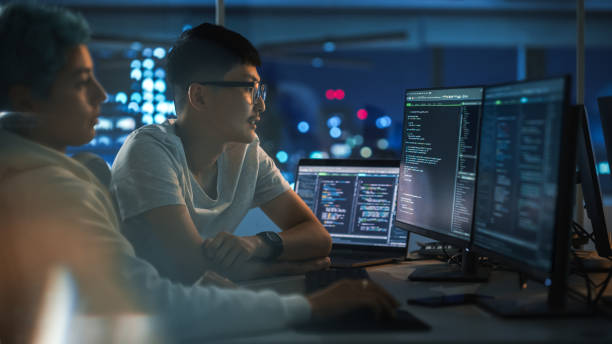 istock Teamwork In Diverse Office at Night: Project Manager Talks with Creative Solutions Specialist, They Discuss App Code Computer. Young Professionals Programming, Create e-Commerce Software 1356364260