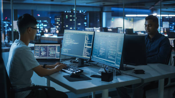 istock Night Office: Young Japanese Man in Working on Desktop Computer. Diverse Multi-Ethnic Team of Programmers Typing Code, Creating Modern Software, e-Commerce App Design, e-Business Programming. 1356364264