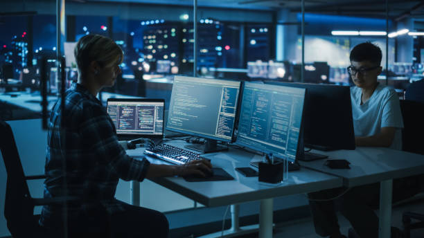 istock Diverse Teamwork in Office at Night: Motivated Woman with Disability Using Prosthetic Arm to Work on Computer. Specialist uses Myoelectric Bionic Hand. Software Engineers work Late on Innovative App 1356364319