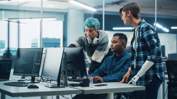 istock Team Meeting In Diverse Office: Project Manager with Disability points Prosthetic Arm at Computer Screen Talks with Multi-Ethnic Specialists. Software Engineers Collaborate on Creative Solution 1356364328