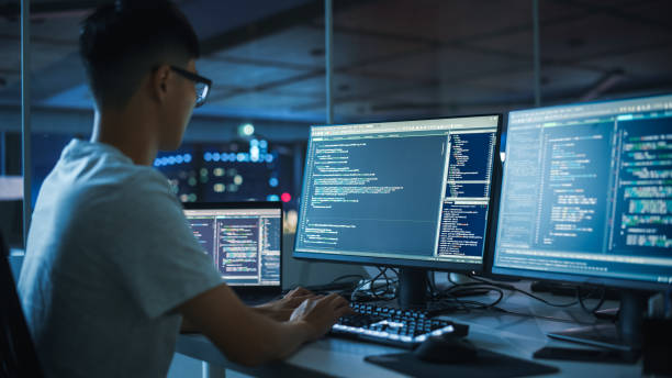 istock Night Office: Young Japanese Man in Working on Desktop Computer. Diverse Multi-Ethnic Team of Programmers Typing Code, Creating Modern Software, e-Commerce App Design, e-Business Programming. 1356364401