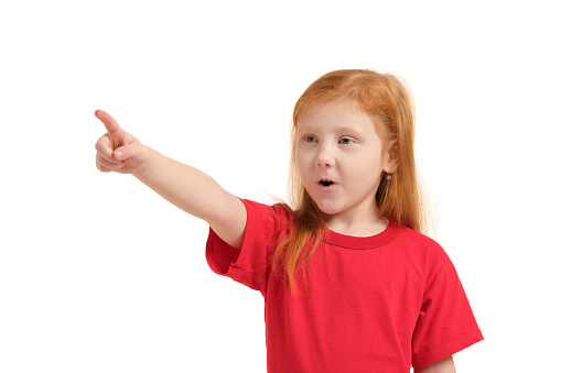 Education, school and imaginary screen concept - cute little girl in a red t-shirt pointing in the air or imaginary screen. Children's emotions
