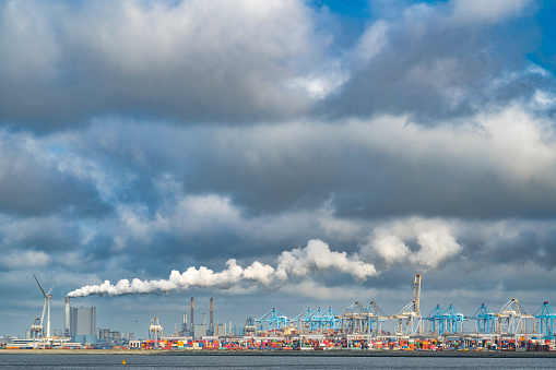Industrial landscape in the port of Rotterdam with a shipping container terminal and energy power plant and clouds above for copy space.