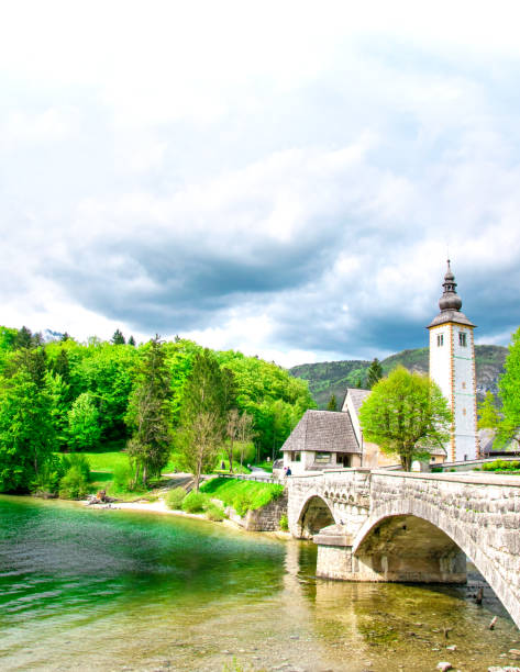 beautiful view of the mountains and green meadows. in the background there is an old church. slovenia - julian alps mountain lake reflection imagens e fotografias de stock