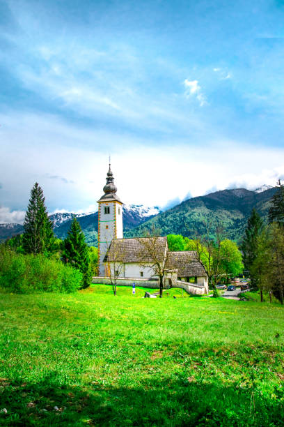 beautiful view of the mountains and green meadows. in the background there is an old church. slovenia - julian alps mountain lake reflection imagens e fotografias de stock