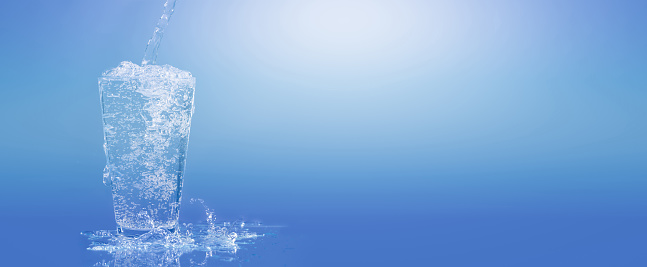 pouring water into a water glass, isolated drinking glass in front of a bright blue sunny and abstract background, close-up of a carbonated refreshing mineral water, beautiful concept with copy space