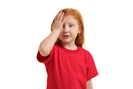 Portrait of cute redhead emotional little girl in red t-shirt isolated on a white, facemalming. Beautiful studio portrait of female little caucasian person