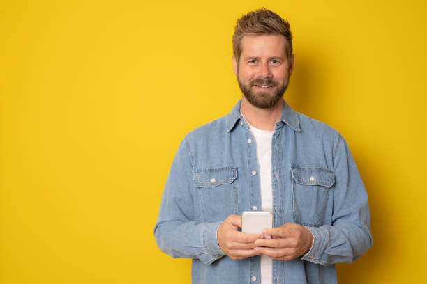 istock Young handsome man holding smartphone in hands, looking at camera with positive smile 1356371126