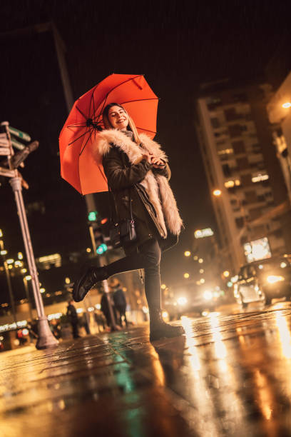istock Happy woman with umbrella downtown at night 1356372132
