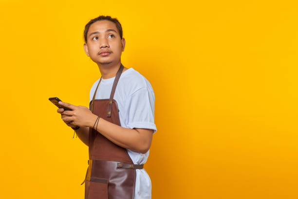 istock Portrait of happy young Asian man using smartphone and looking at empty space on yellow background 1356372477