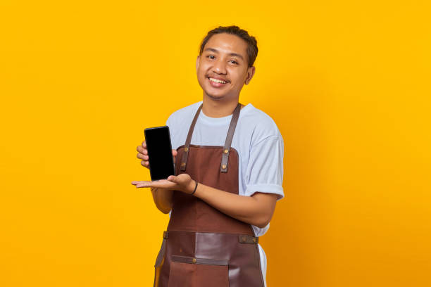 istock Cheerful Asian man showing smartphone blank screen over yellow background 1356373746