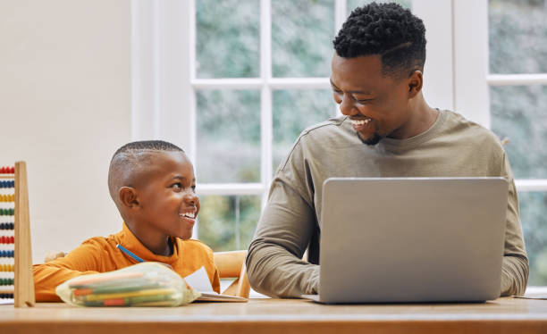 istock Shot of a young father using a laptop while his son does homework at home 1356374130